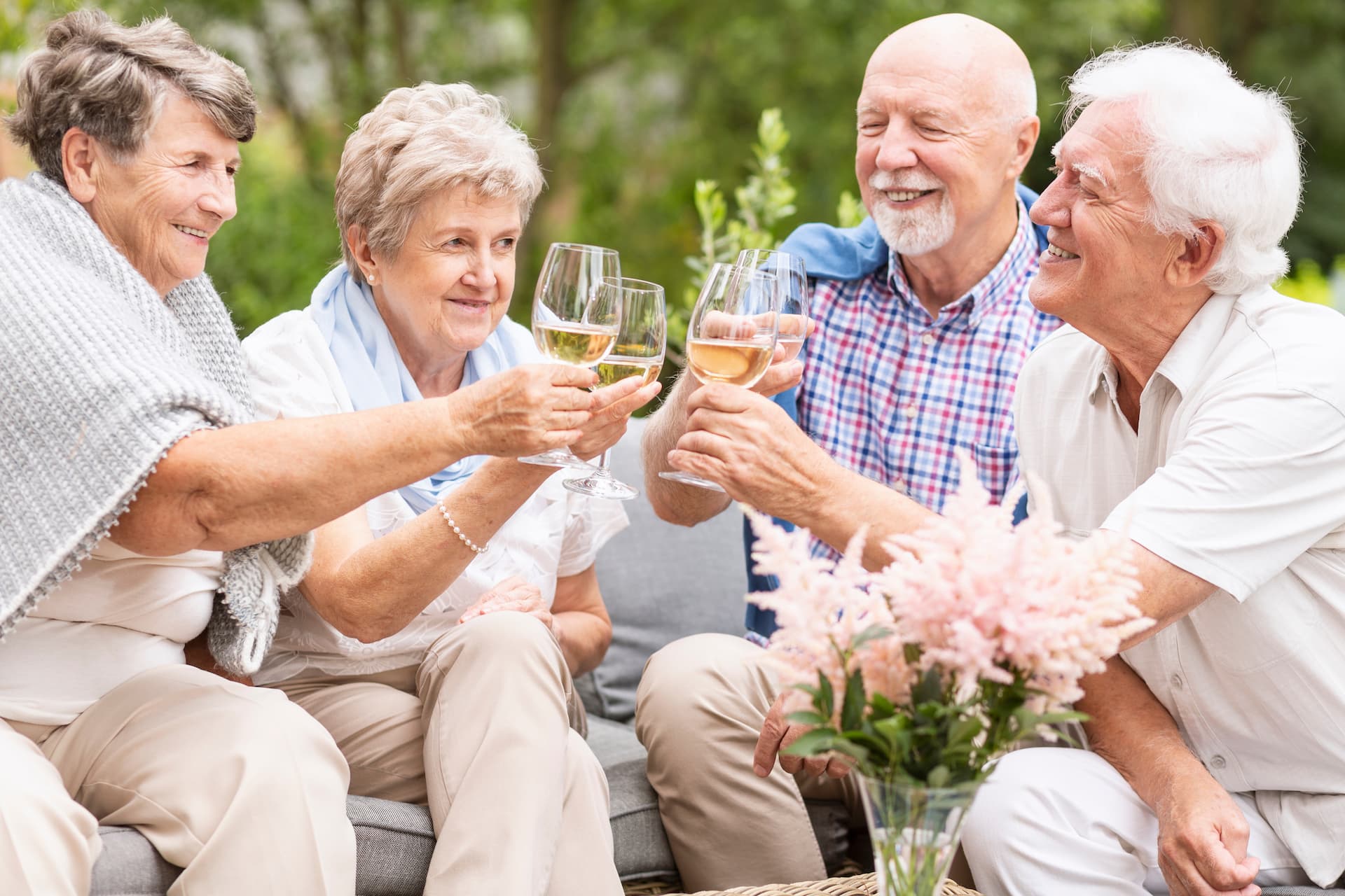 four seniors laughing and toasting wine glasses outdoors